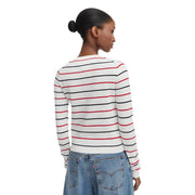 Eine Frau trägt einen weißen, gestreiften, langärmeligen Rundhalspullover von Tommy Hilfiger aus Bio-Baumwolle.