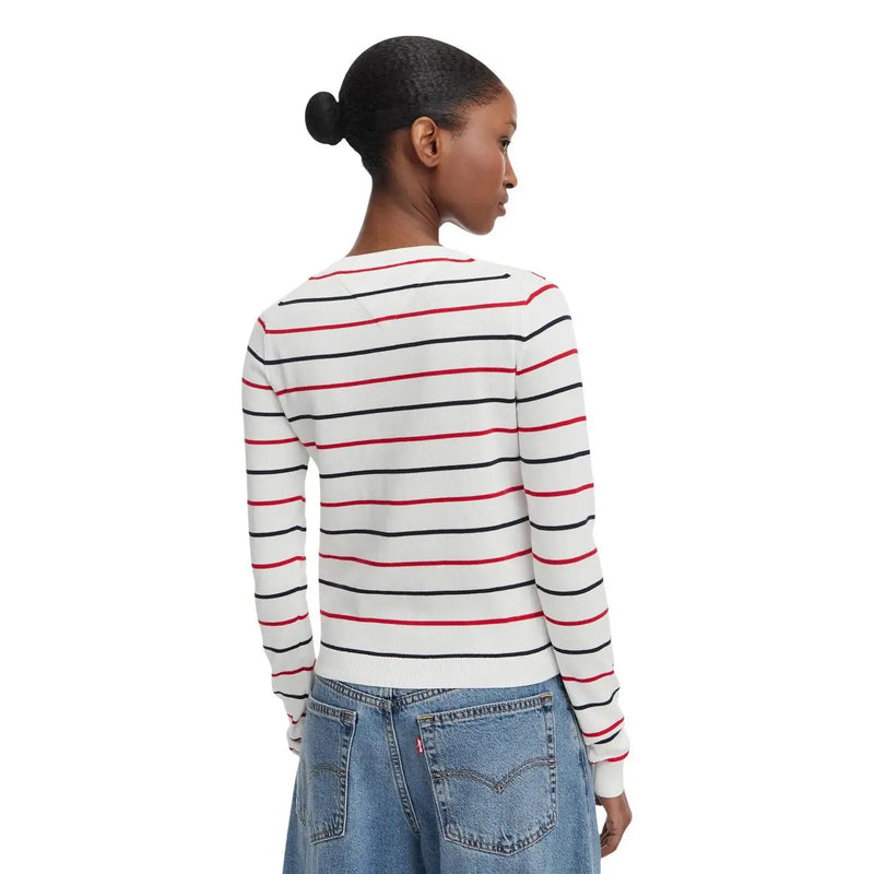 Eine Frau trägt einen weißen, gestreiften, langärmeligen Rundhalspullover von Tommy Hilfiger aus Bio-Baumwolle.