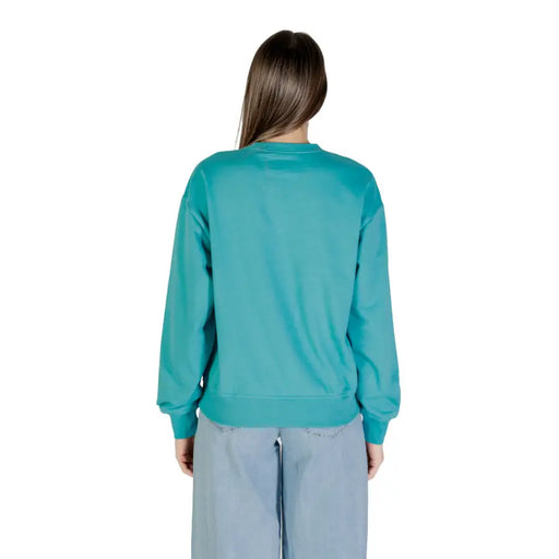Woman wearing Calvin Klein Jeans teal crewneck sweatshirt and light blue wide-leg pants
