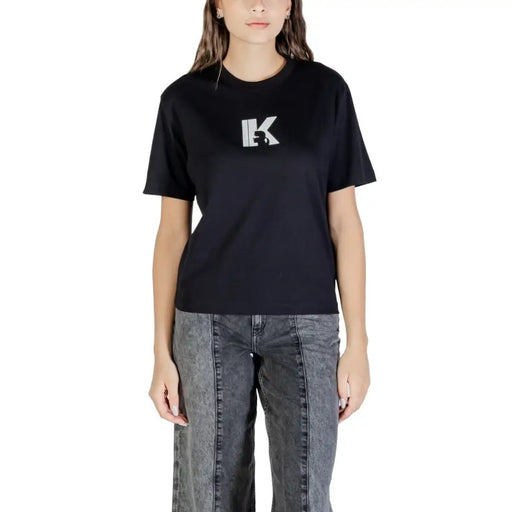 Woman wearing black crew-neck T-shirt with white K graphic and dark wash wide-leg jeans