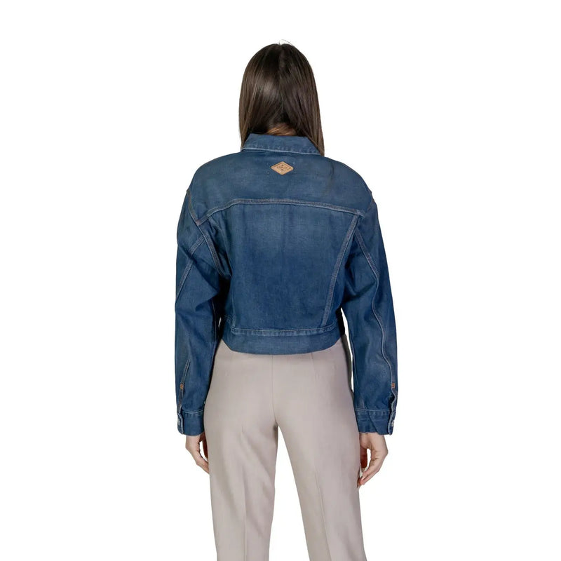 Back side of women’s denim zip up blazer showing blue denim cropped jacket with brown leather patch on back collar
